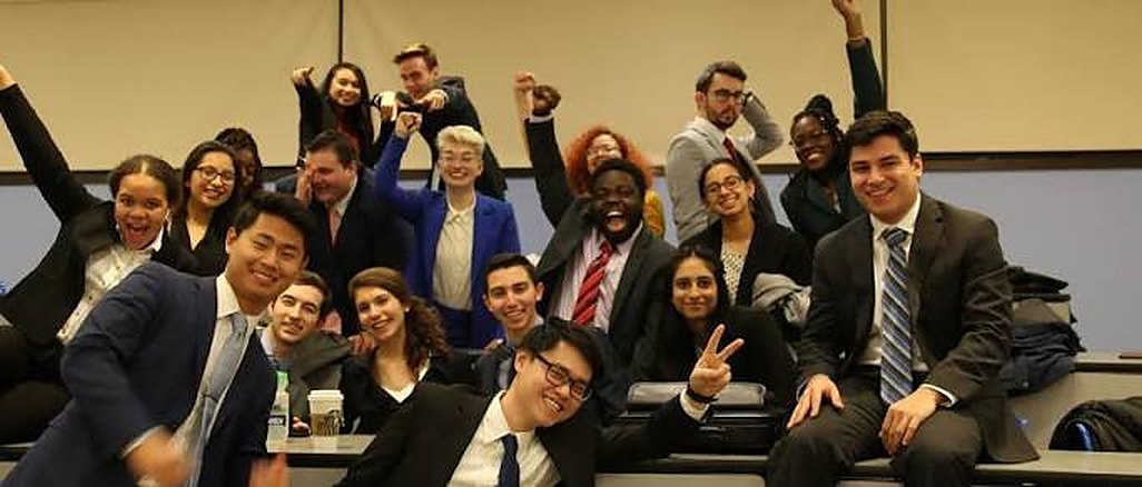 A large group of students in suits celebrating together in a lecture hall