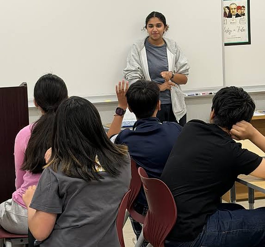 A coach leading a classroom session while a student raises a hand