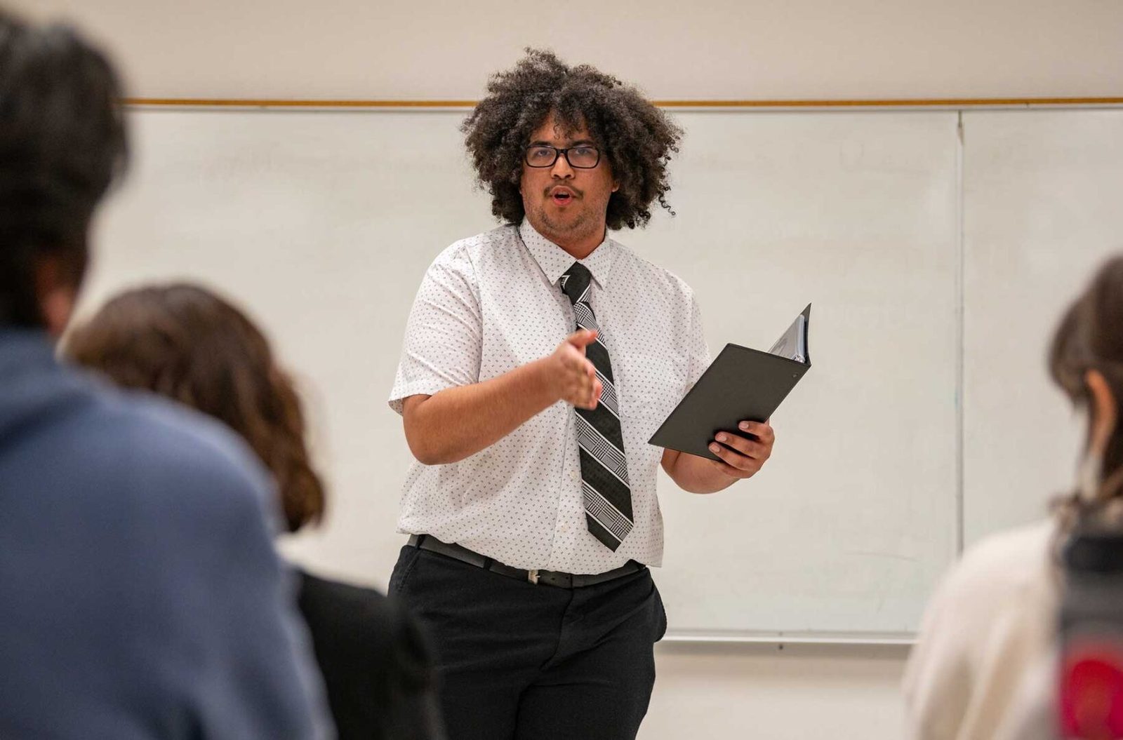 A student delivering a speech from a binder in front of a class